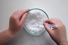 two hands are scooping sugar into a glass bowl with a white spoon in it