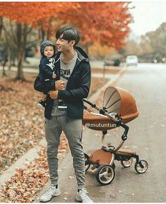 a man holding a baby in his arms while standing next to a stroller on the street