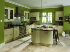 a large kitchen with green walls and white cabinets, an island in the middle is surrounded by stools