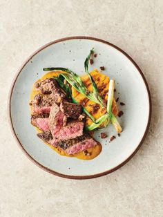 a white plate topped with meat and veggies on top of a marble table