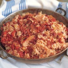 a pan filled with rice and meat sitting on top of a white cloth covered table