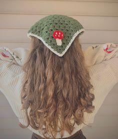 the back of a woman's head wearing a crocheted hat with a red mushroom on it