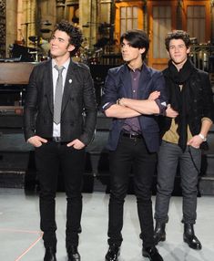 three young men standing next to each other in front of a stage with microphones