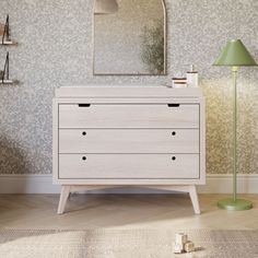 a white dresser sitting next to a green lamp