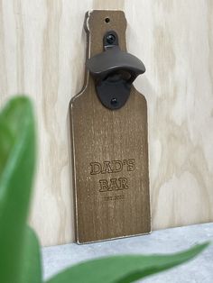 a bottle opener hanging from the side of a wooden wall next to a green plant