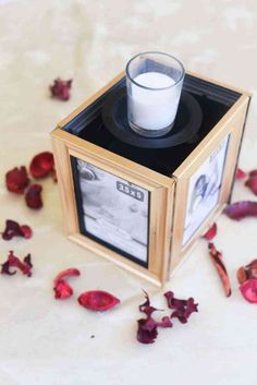 a small wooden box with a candle and rose petals scattered around it on a table