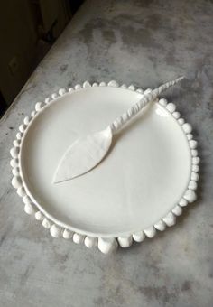 a white plate with a leaf on it sitting on a counter top next to a knife