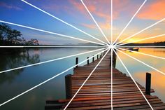 a wooden dock sitting on top of a lake under a colorful sky with lines going through it