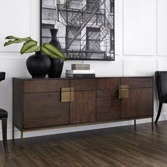 a black vase and two chairs in a room with white walls, wood flooring and a painting on the wall