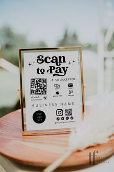 a sign that says scan to pay sitting on top of a wooden table next to a white feather