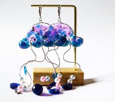 a pair of earrings that have been made out of glass beads and other items on a wooden stand