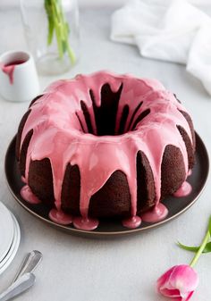 a chocolate bundt cake with pink icing on a plate next to a flower