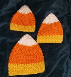 three crocheted hats are laying on a black surface, one is orange and the other is white