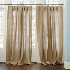 the curtains are hanging in front of two windows with wood floors and blue walls behind them