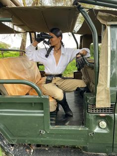 a woman is sitting in the driver's seat of a green jeep with a cow