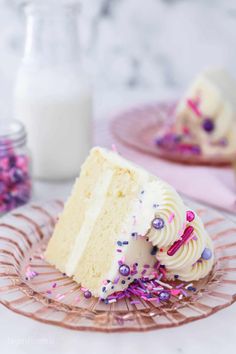 a slice of white cake with sprinkles on a glass plate next to a bottle of milk