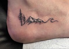 a small tattoo on the foot of a person with mountains and trees in the background