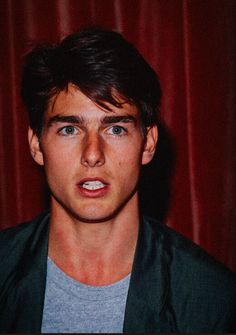 a young man is making a face with his tongue out in front of a red curtain