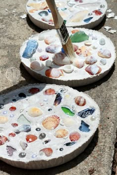 two seashell mosaics are sitting on the ground with a paintbrush in them