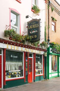 there are many shops on the street with flowers growing out of their windows and above them is a sign that says rue lauries pub