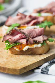 a wooden cutting board topped with sandwiches on top of a white table covered in green leafy garnish