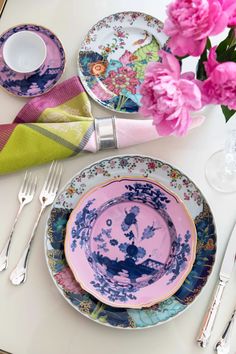 the table is set with plates, silverware and pink flowers