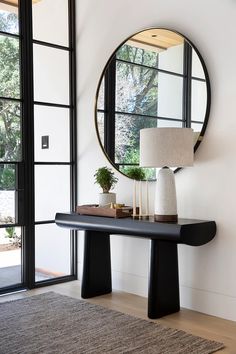 a black table with a mirror and lamp on it in front of a large window