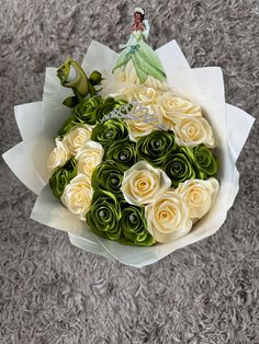 a bouquet of white and green roses with a little fairy on top is sitting on the floor