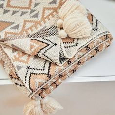 a blanket with tassels on it sitting on top of a white table next to a window