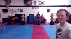 a man standing on top of a blue mat in a gym next to other people