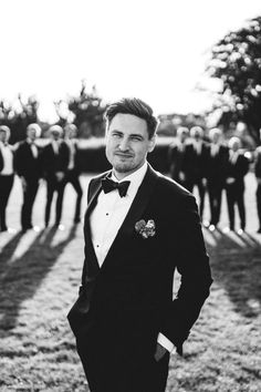 a man in a tuxedo is posing for the camera with other men behind him