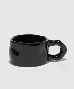 a black coffee cup sitting on top of a white table