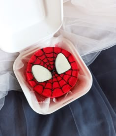 a spider - man cake in a plastic container on a blue bed with white netting