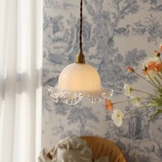 a white lamp hanging from a ceiling in a room with floral wallpaper and flowers