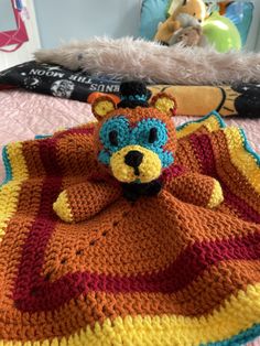 a crocheted teddy bear laying on top of a blanket