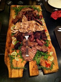 a wooden cutting board topped with meat and veggies on top of a table