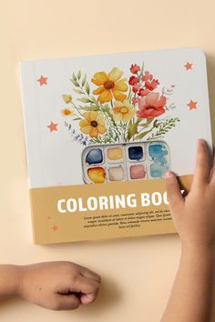 a child's hand is holding an art book with watercolors on it