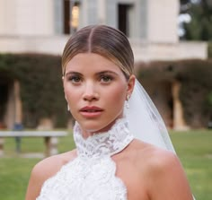 a woman wearing a wedding dress and veil in front of a large building with trees