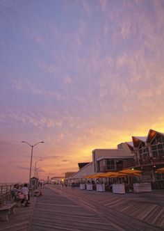 people are sitting on benches at the end of a boardwalk as the sun goes down