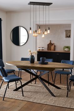 a dining room table with blue chairs and a round mirror on the wall above it