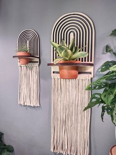 two wall hangings with plants and potted plants on them in front of a gray wall