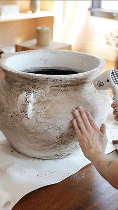 a person is using a hair dryer on a large pot that has been turned into a vase