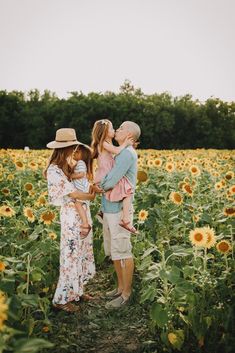 three people standing in a field of sunflowers with one person holding the other