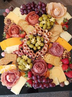 an assortment of cheeses, crackers, grapes and strawberries on a black platter