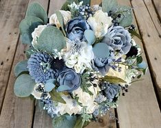 a bridal bouquet with blue and white flowers on a wooden table in front of wood planks