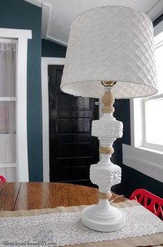 a white lamp sitting on top of a wooden table next to a red dining room chair