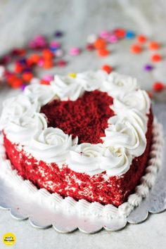 a heart shaped red velvet cake with white frosting and sprinkles on top