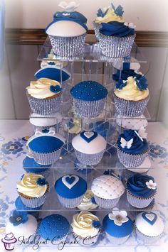 cupcakes in blue and white frosting are arranged on a clear cake stand