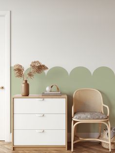 a white dresser sitting next to a wooden chair in front of a green painted wall