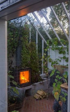 an outdoor fireplace is lit in the middle of a patio with brick flooring and greenery surrounding it